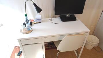 Un bureau blanc avec un écran d’ordinateur, une lampe, une bouteille d’eau, une boîte de mouchoirs et une poubelle.