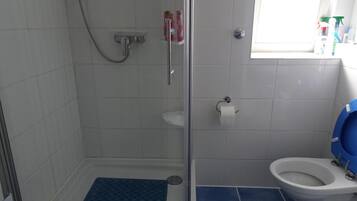Kylpyhuone, jossa on suihku, wc ja pieni ikkuna.