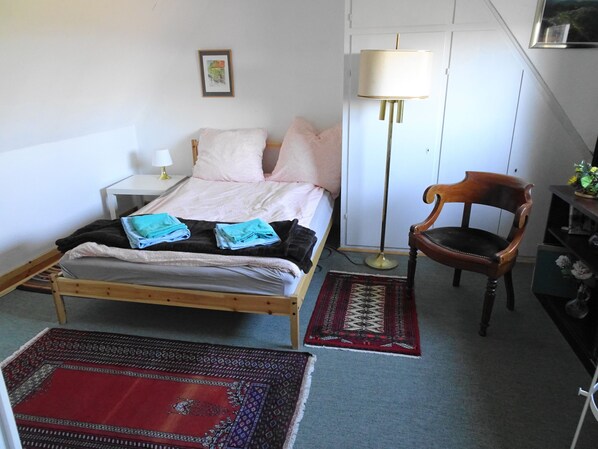Une chambre à coucher bien rangée, avec un lit, une table de chevet, une lampe, une chaise et des tapis.