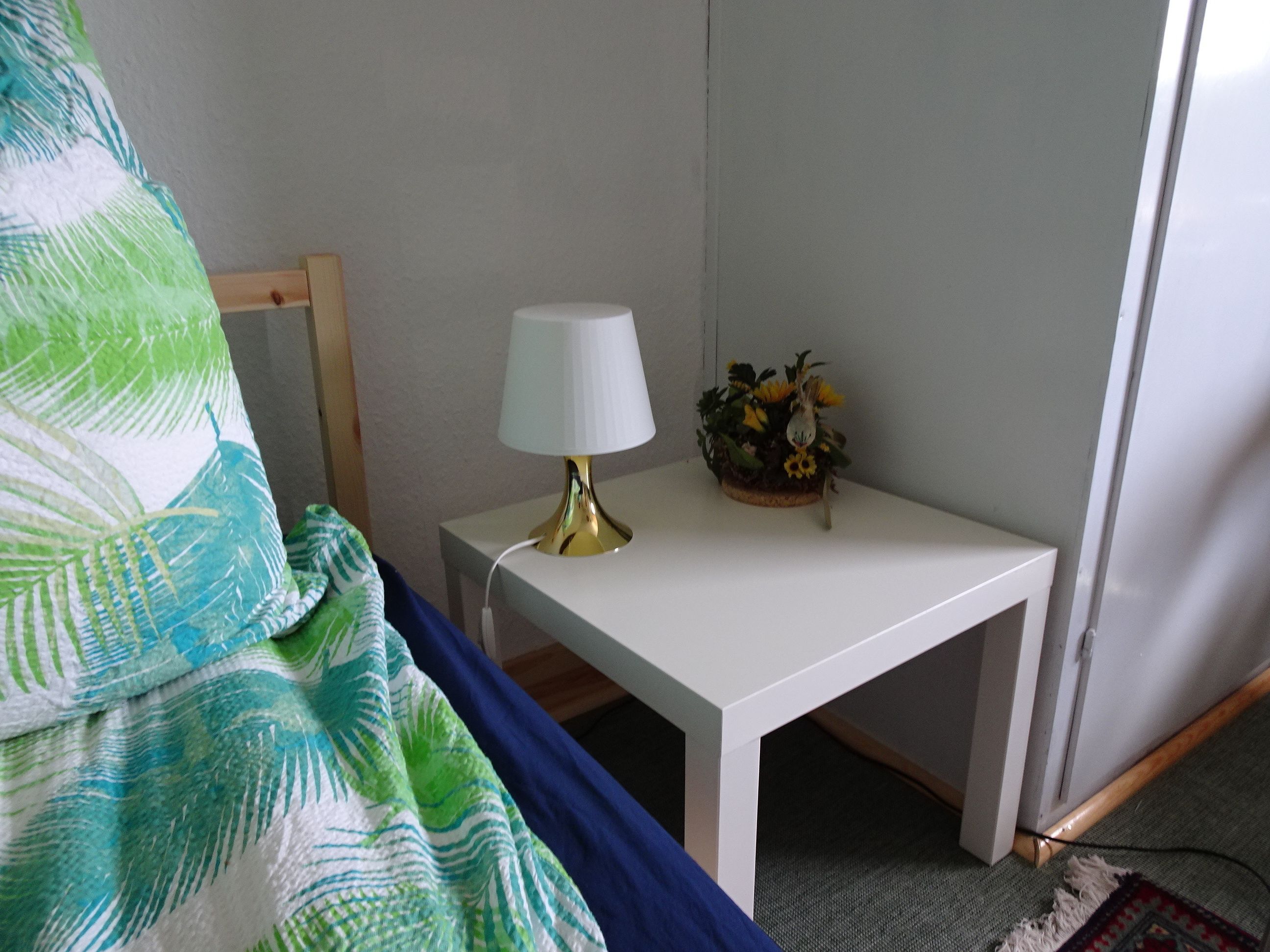 Een klein wit nachtkastje met een lamp en een klein plantje.