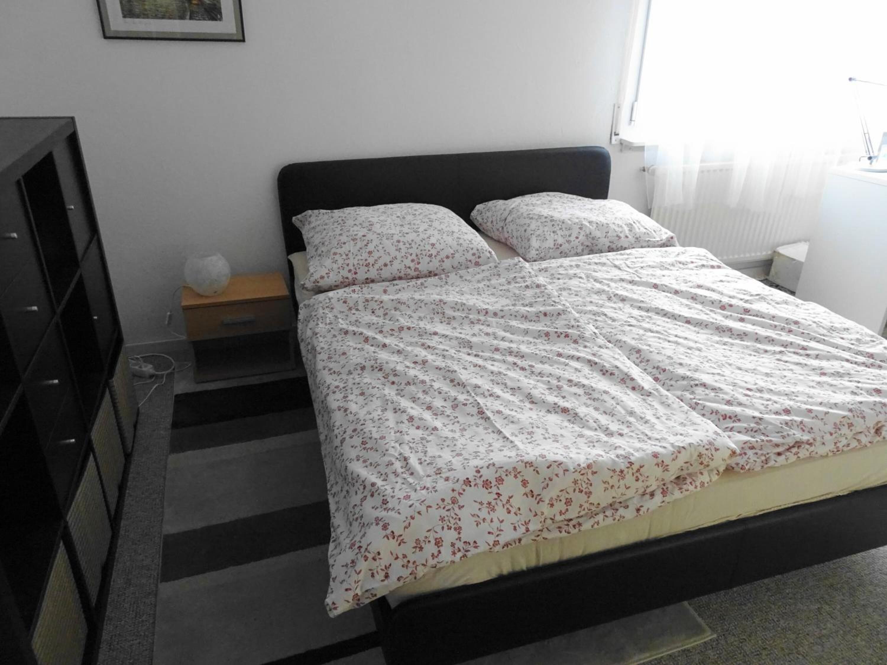 Un dormitorio con cama, mesita de noche, cómoda y ventana con cortinas.