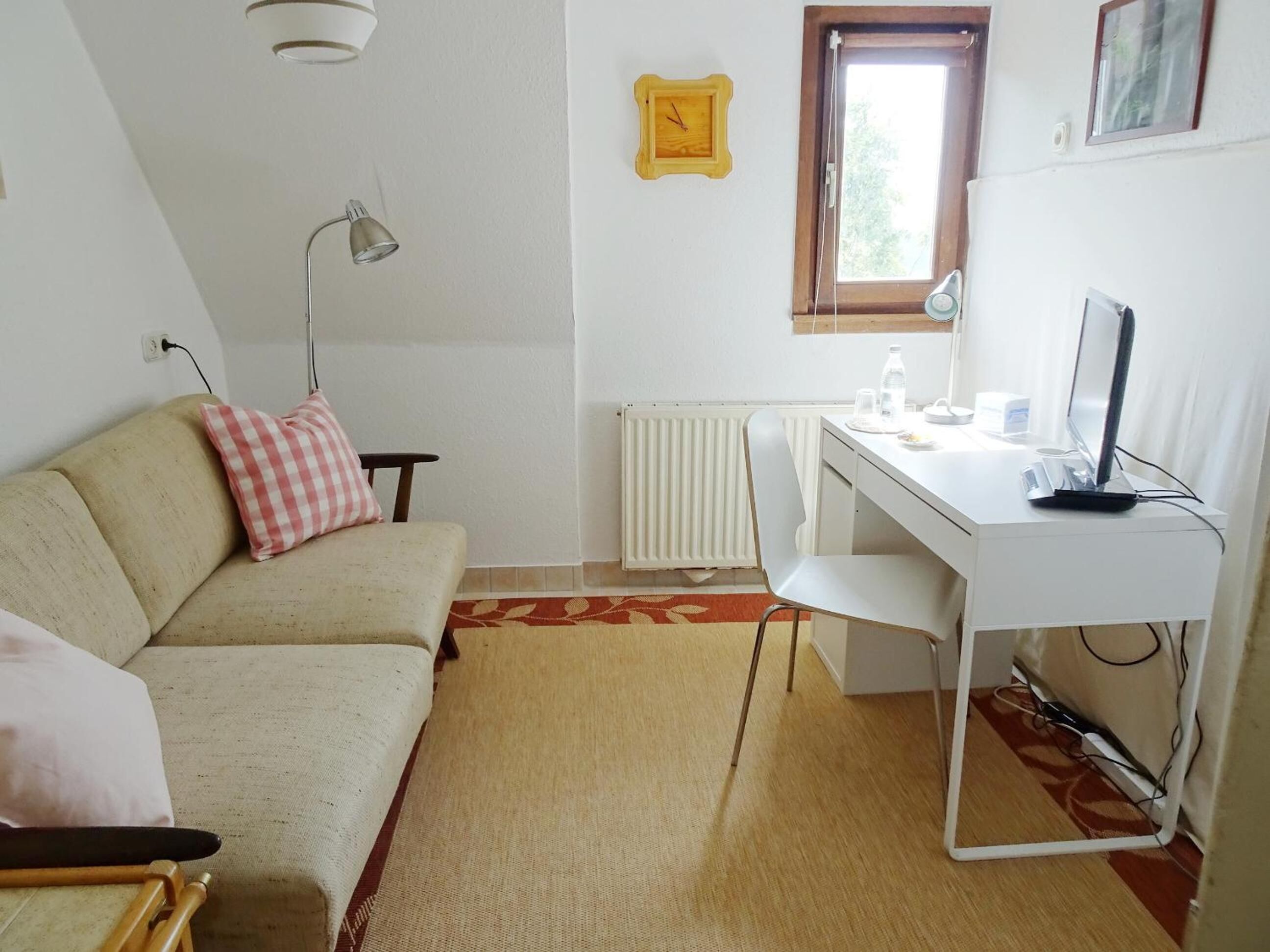 A small, well-lit room with a white desk, a beige sofa, and a radiator.