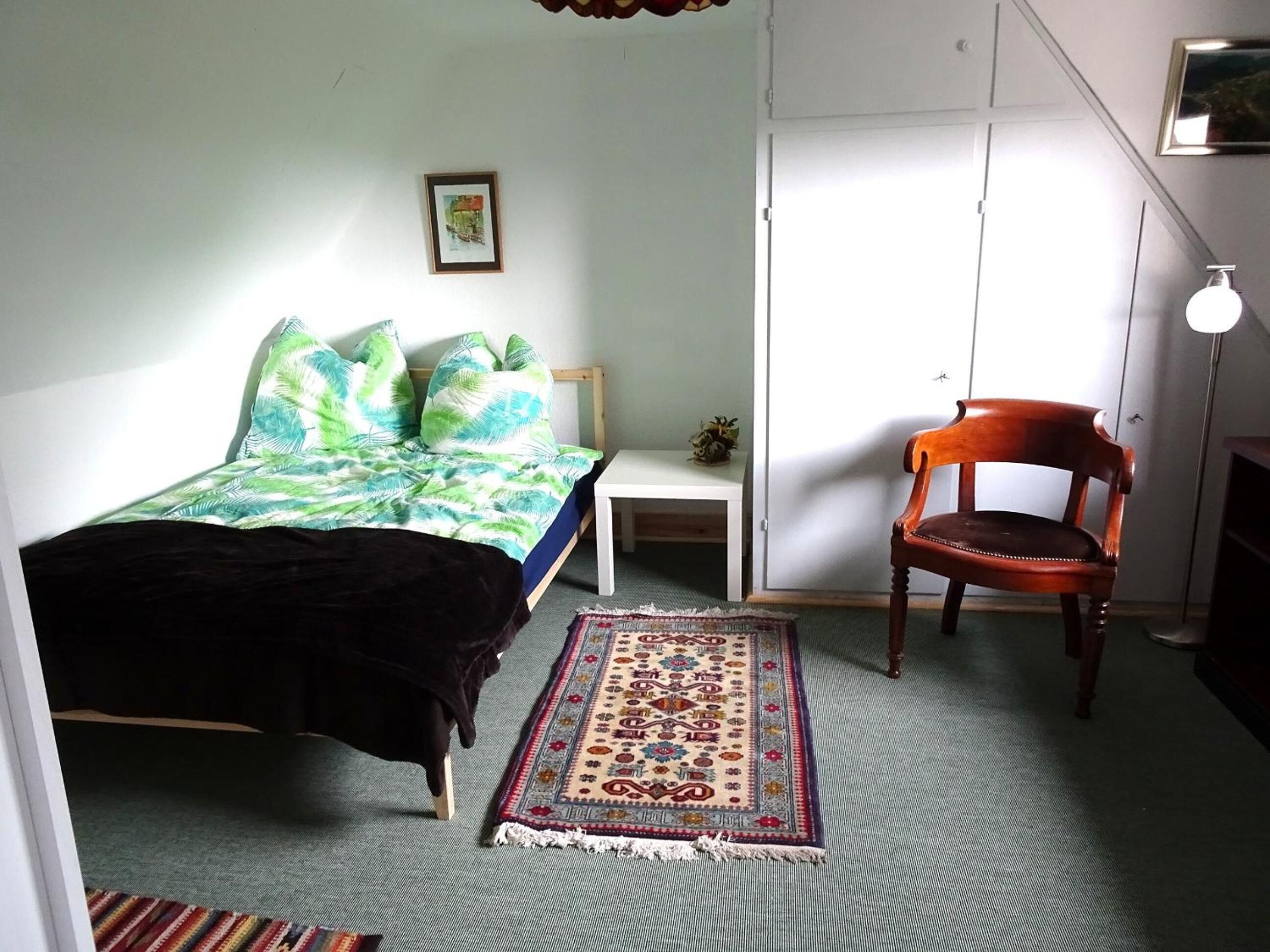 Ein Schlafzimmer mit Bett, einem Sessel, einem kleinen Tisch, einem Teppich und einem Kleiderschrank.