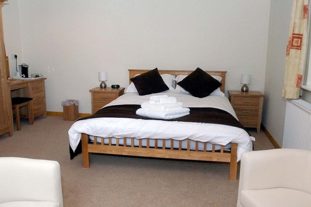 A neatly arranged bedroom with a wooden bed, two bedside tables with lamps, a small desk, and a chair.