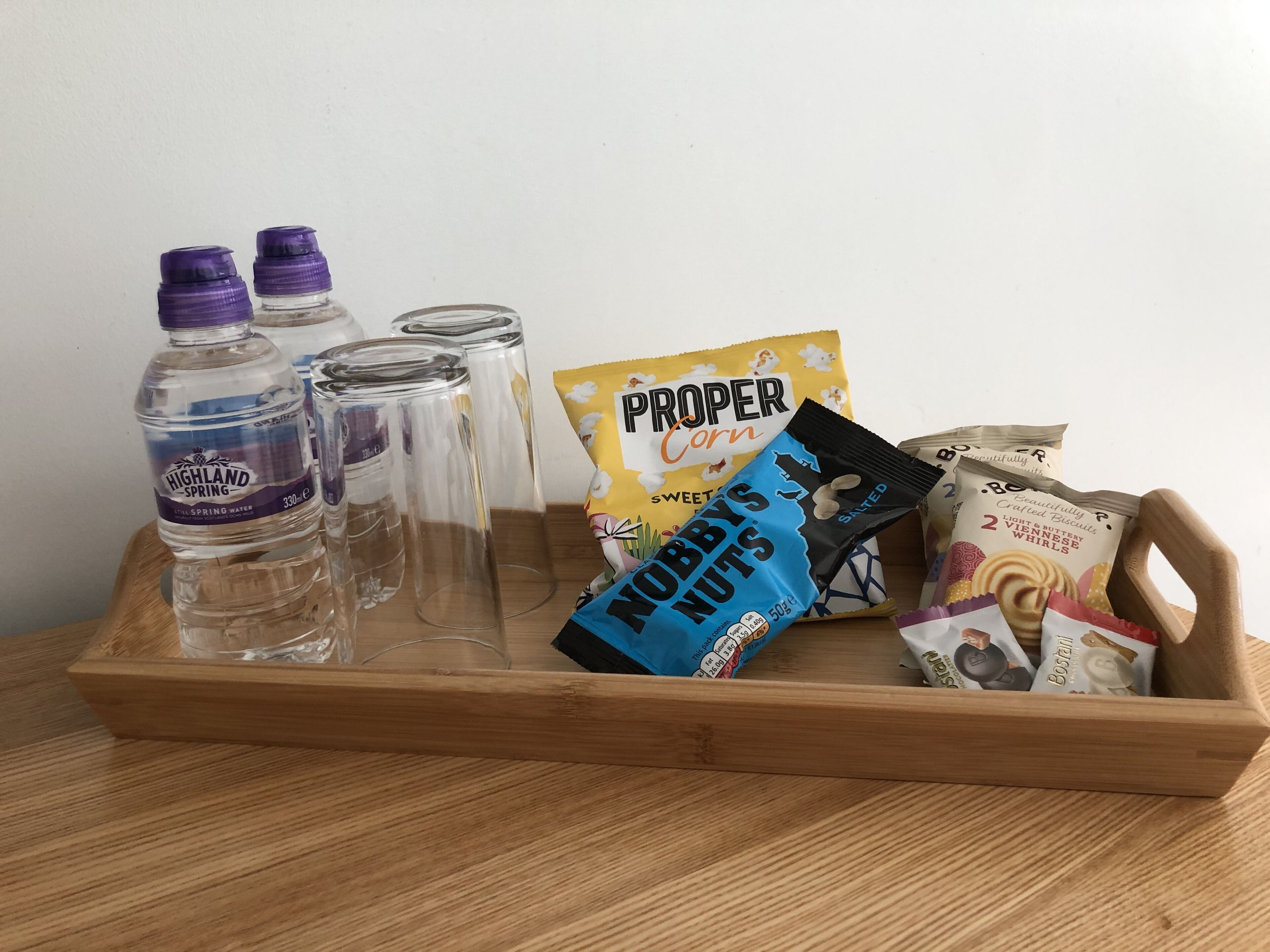 A wooden tray with water bottles, glass containers, and snack packages.