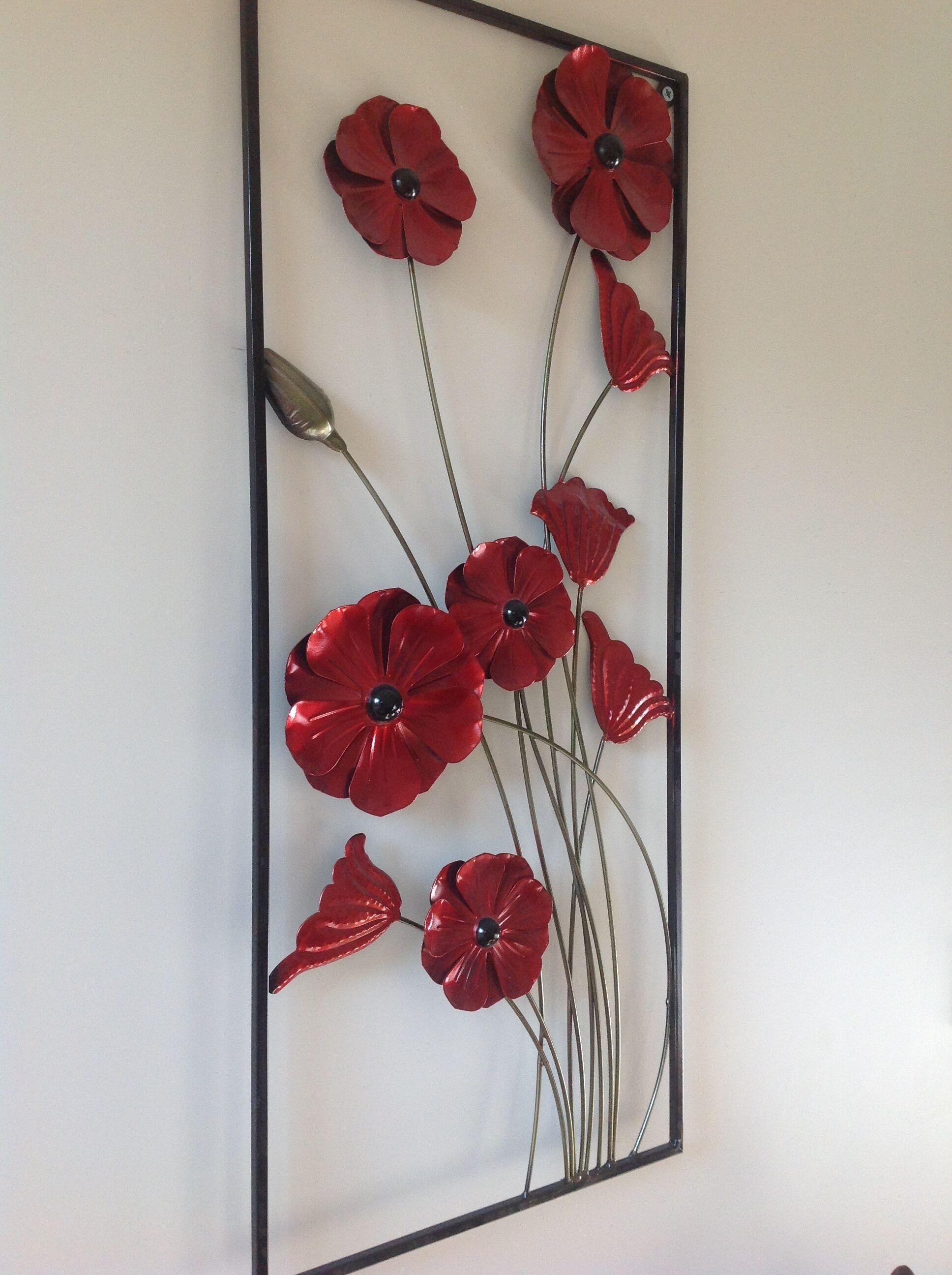 Eine Wanddekoration mit roten Blüten und schwarzen Kernen.