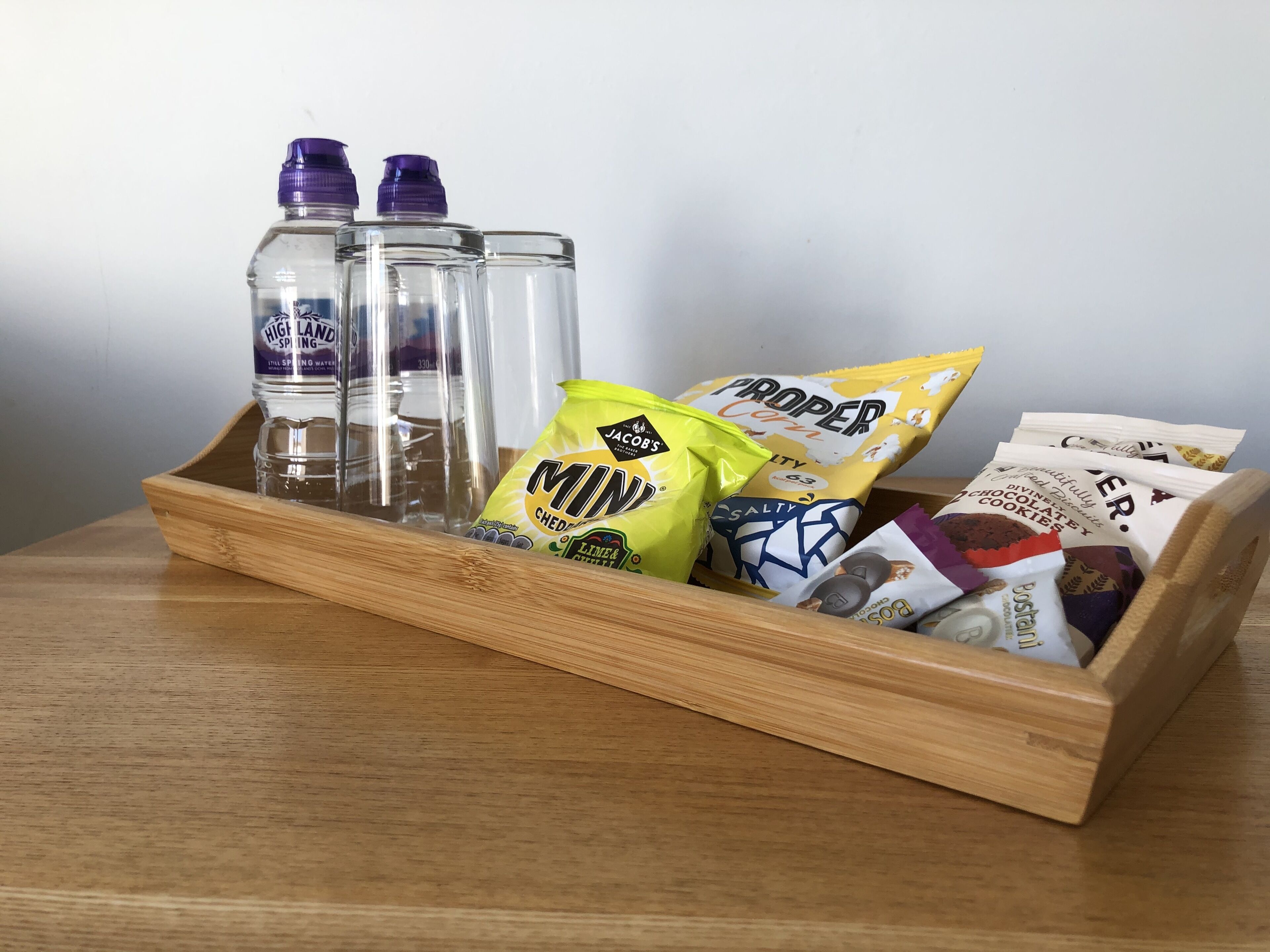 A wooden tray with clear glass bottles, a lime-flavored snack bag, and various snack packets.
