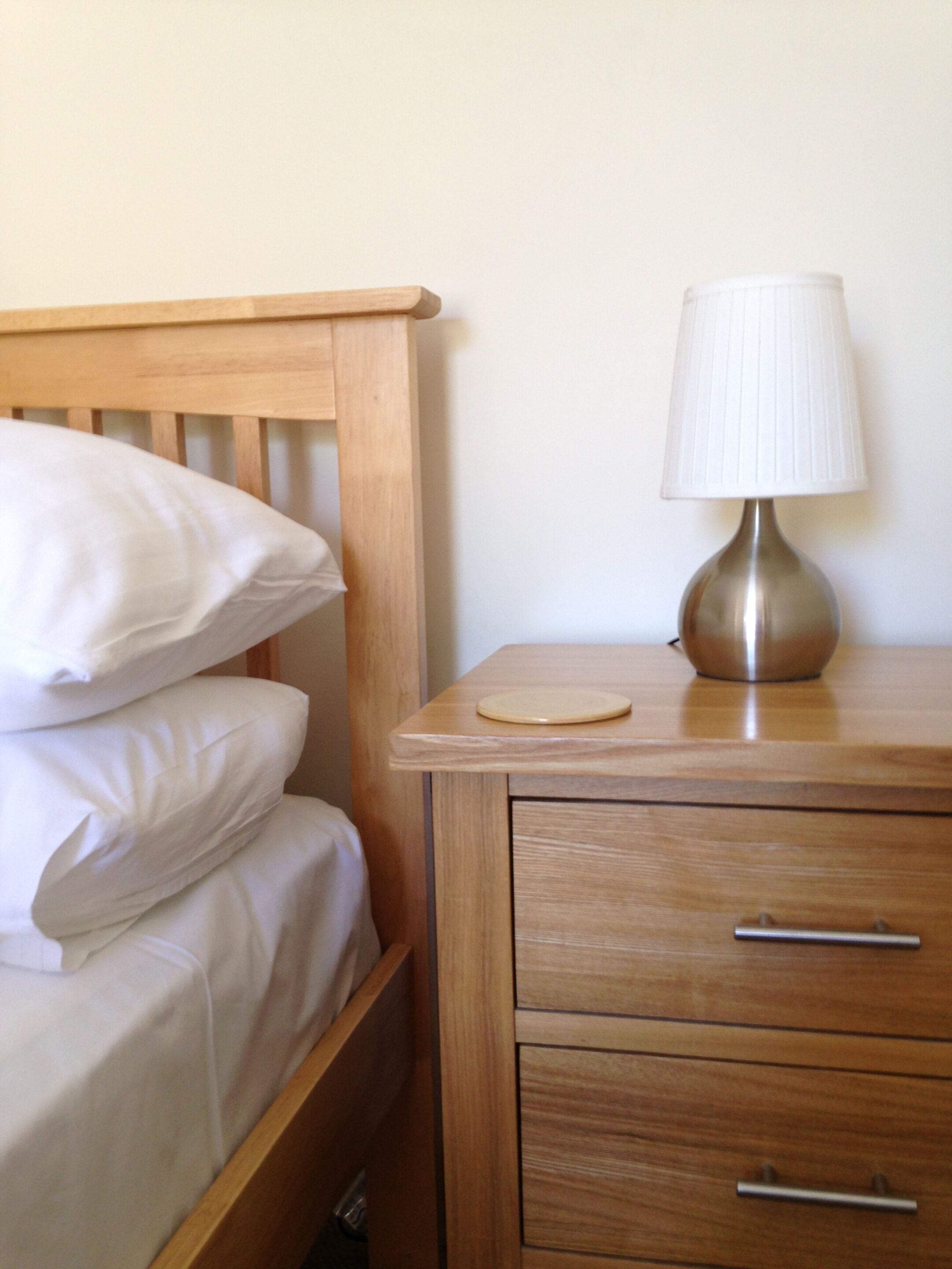 Un lit en bois avec une literie blanche, une table de chevet avec une lampe et une commode.