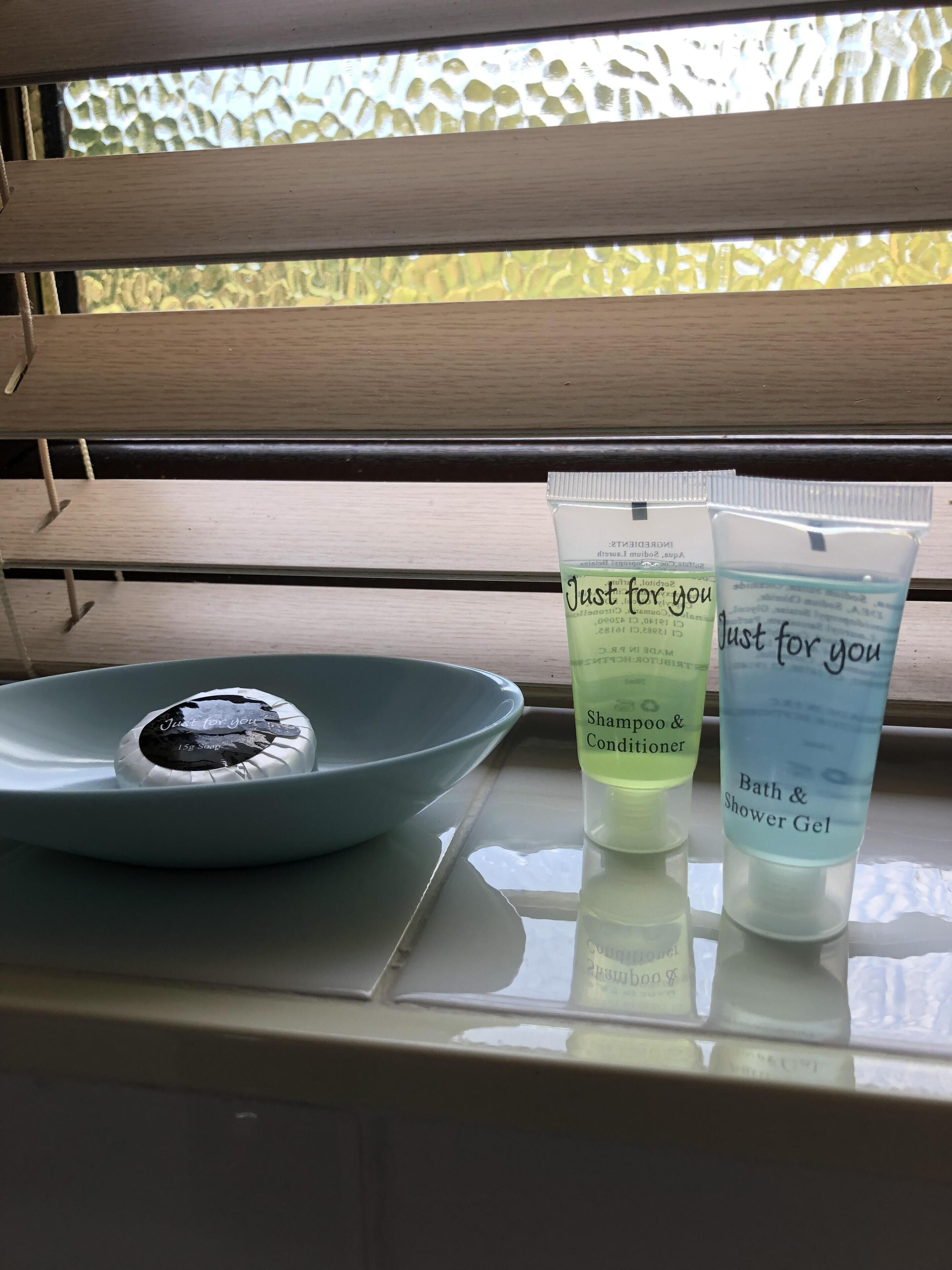 A bathroom counter with a blue bowl containing a bar of soap, two tubes of 'Just for you' bath and shower gel, and a bottle of shampoo and conditioner.