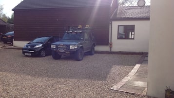 A gravel driveway with two vehicles parked in front of a building with a sloped roof and a satellite dish.