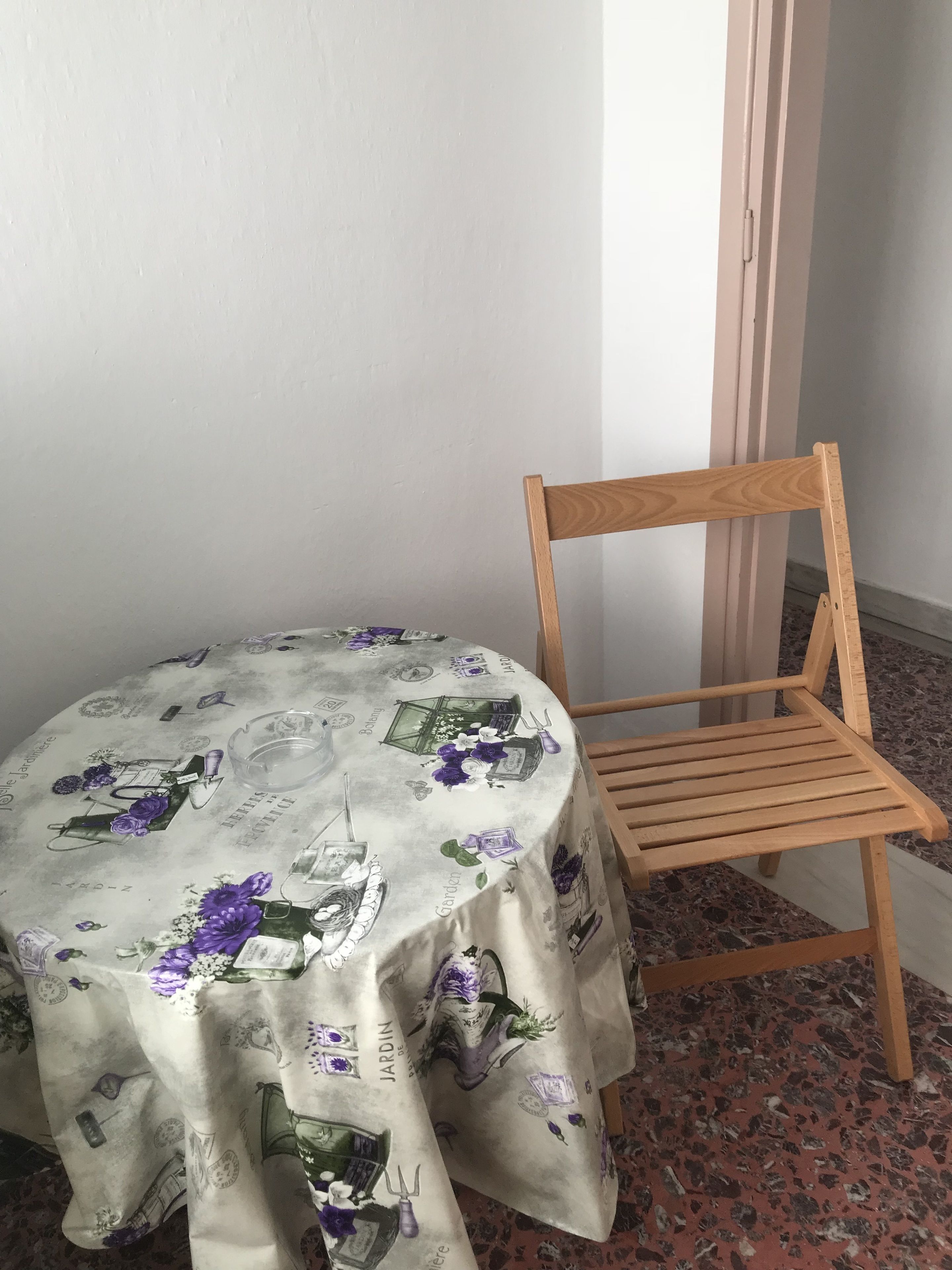 A round table with a floral tablecloth and a wooden chair.