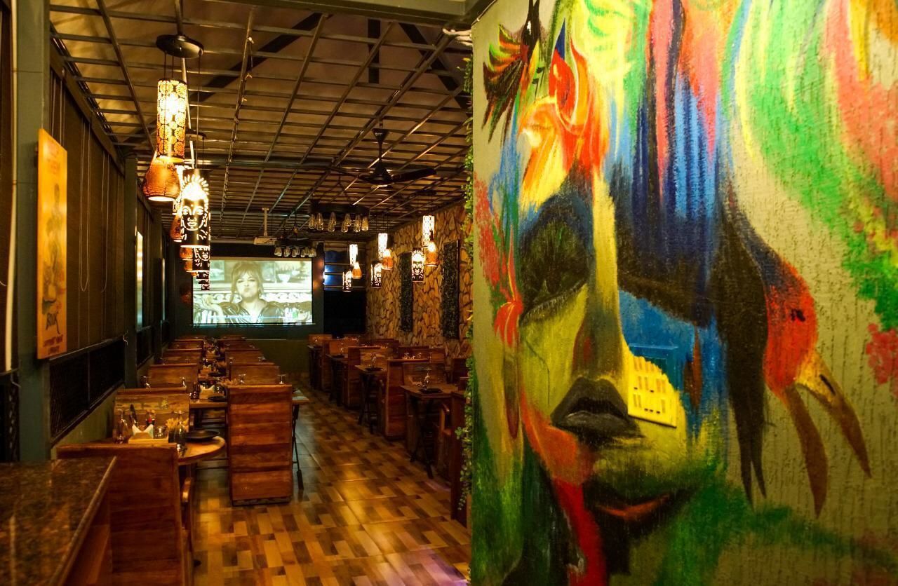 Un restaurante con mesas y sillas de madera, un mural en la pared y lámparas colgantes.
