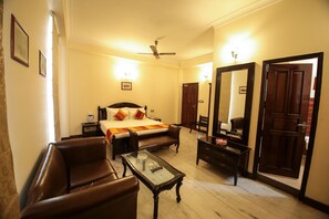 Habitación de hotel con cama, escritorio, silla, mesa de centro, ventilador de techo y un espejo grande.