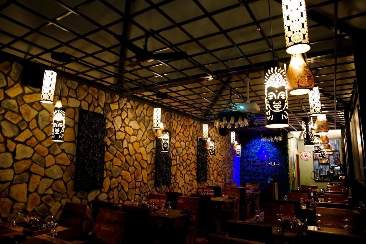 A restaurant interior with stone walls, hanging pendant lights, and a blue-lit wall.