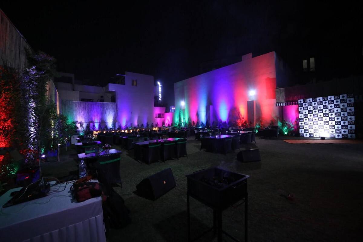 An outdoor event space with tables and chairs, illuminated by colorful lights.