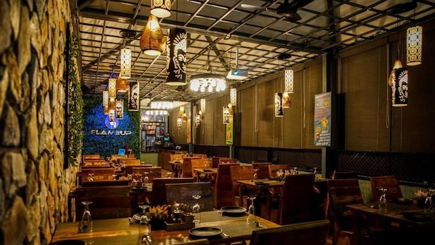 A restaurant interior with wooden tables and chairs, hanging pendant lights, and a neon sign reading "FLAME UP". - JD Hotel Four Boutique (Jaipur)