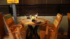 A round wooden table with metal legs, accompanied by two rustic wooden chairs. A sign above the table reads "SUPPORT YOUR LIBRARY." - JD Hotel Four Boutique (Jaipur)