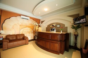 Un área de recepción con un escritorio de madera, una recepcionista, un reloj y un televisor.
