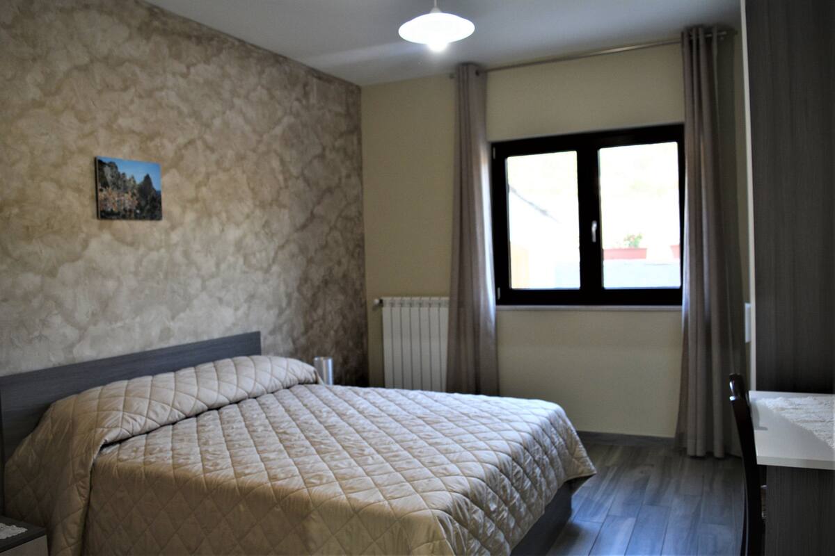 A bedroom with a bed, a radiator, a window with curtains, and a picture on the wall.