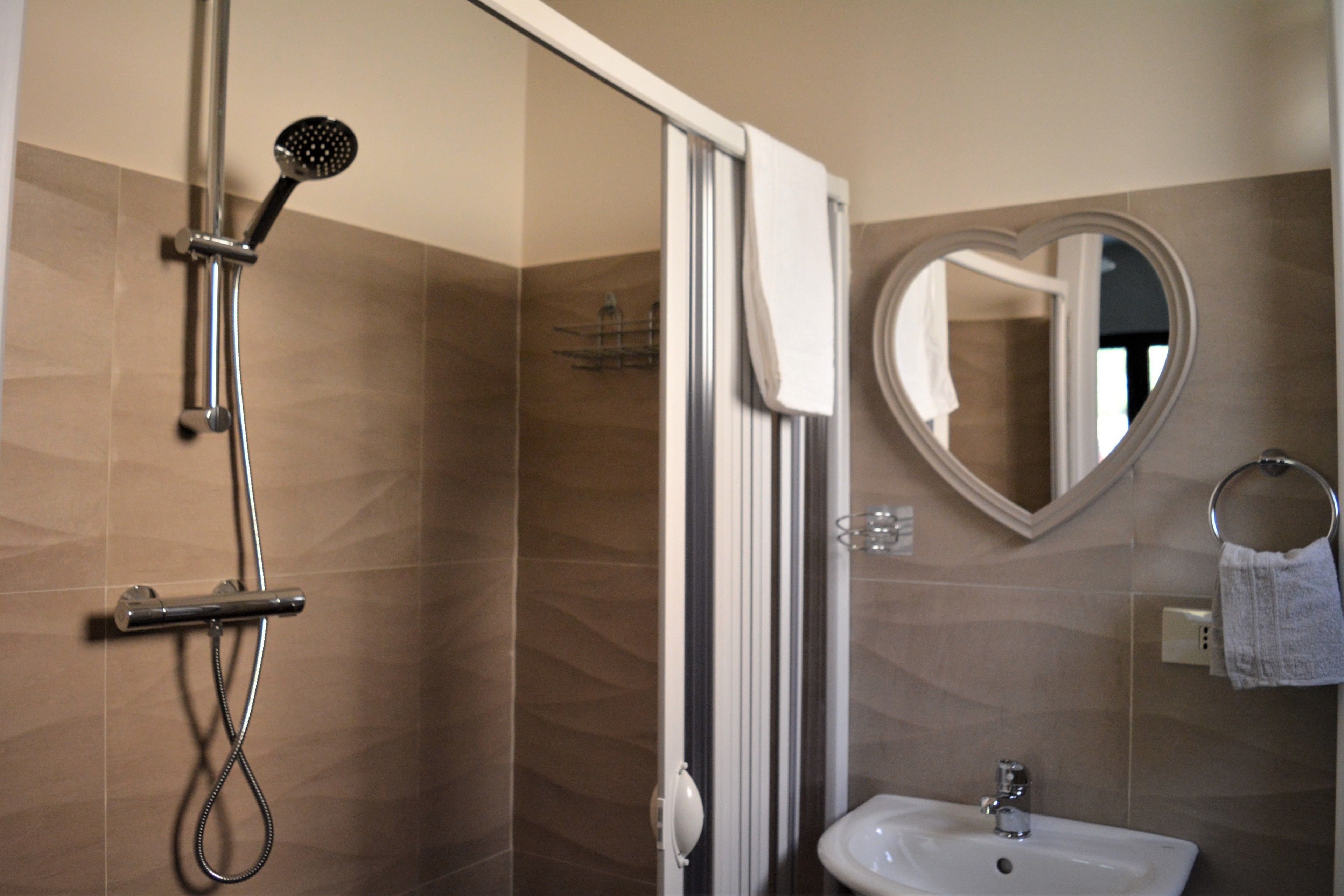 A bathroom with a shower, a sink, and a heart-shaped mirror.