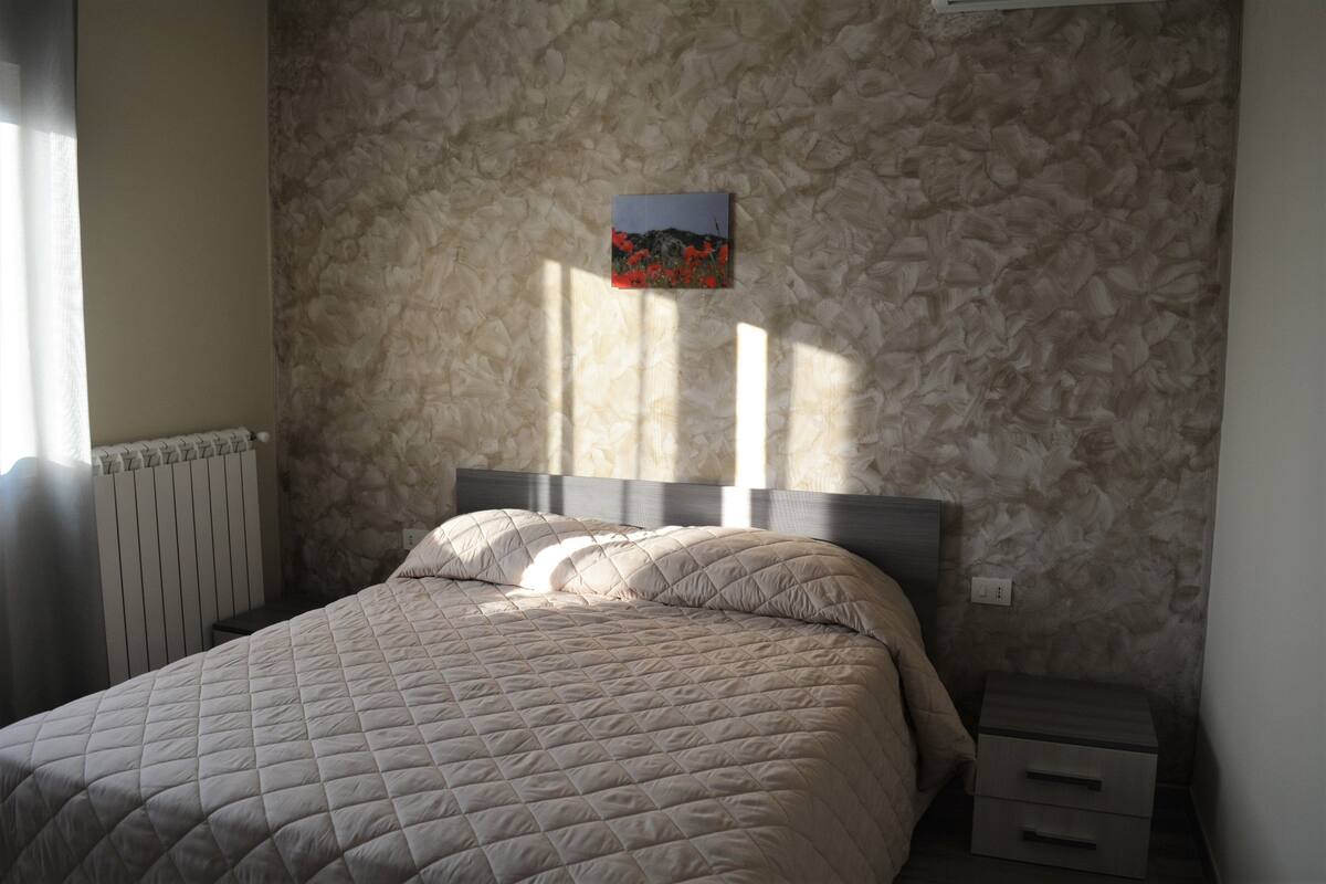A bedroom with a quilted bedspread, a headboard, a nightstand, and a wall-mounted picture.