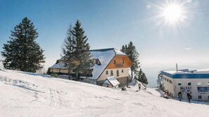 A snow-covered ski resort with a prominent building featuring a sloped roof and a wooden facade. - Hotel Rozka (Cerklje na Gorenjskem)
