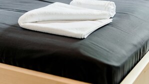 A bed with a black mattress and white sheets, a wooden headboard, and a white towel on the bed. - Hotel Rozka (Cerklje na Gorenjskem)