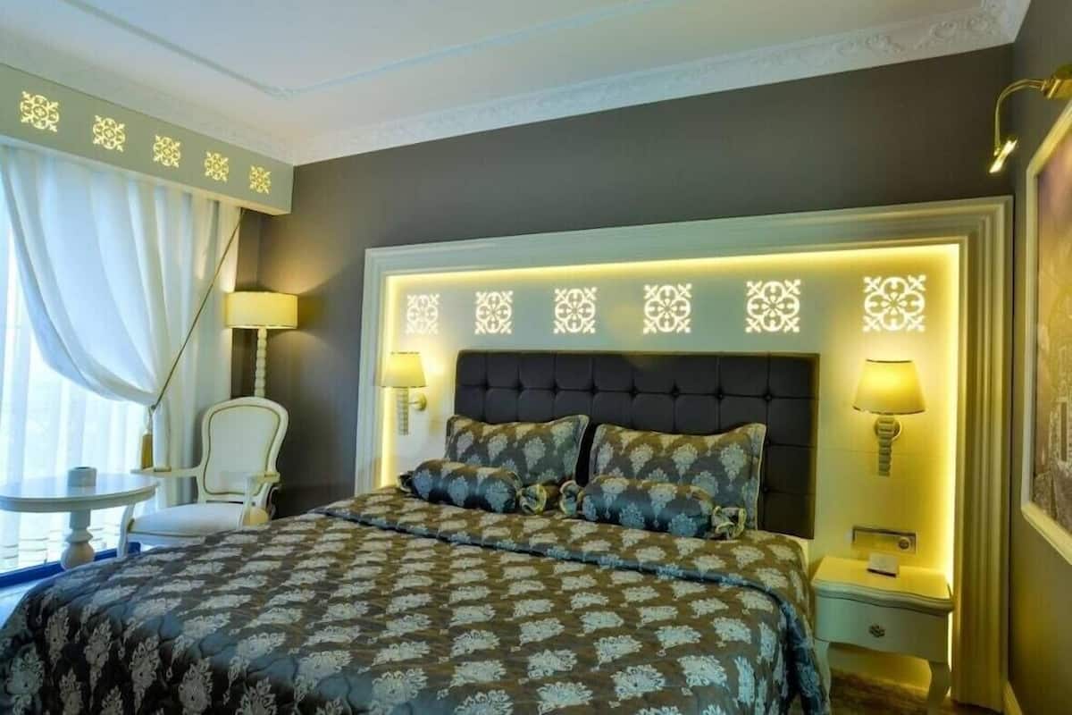 Una habitación de hotel con una cama grande, dos lámparas de noche, una mesita pequeña y una silla.