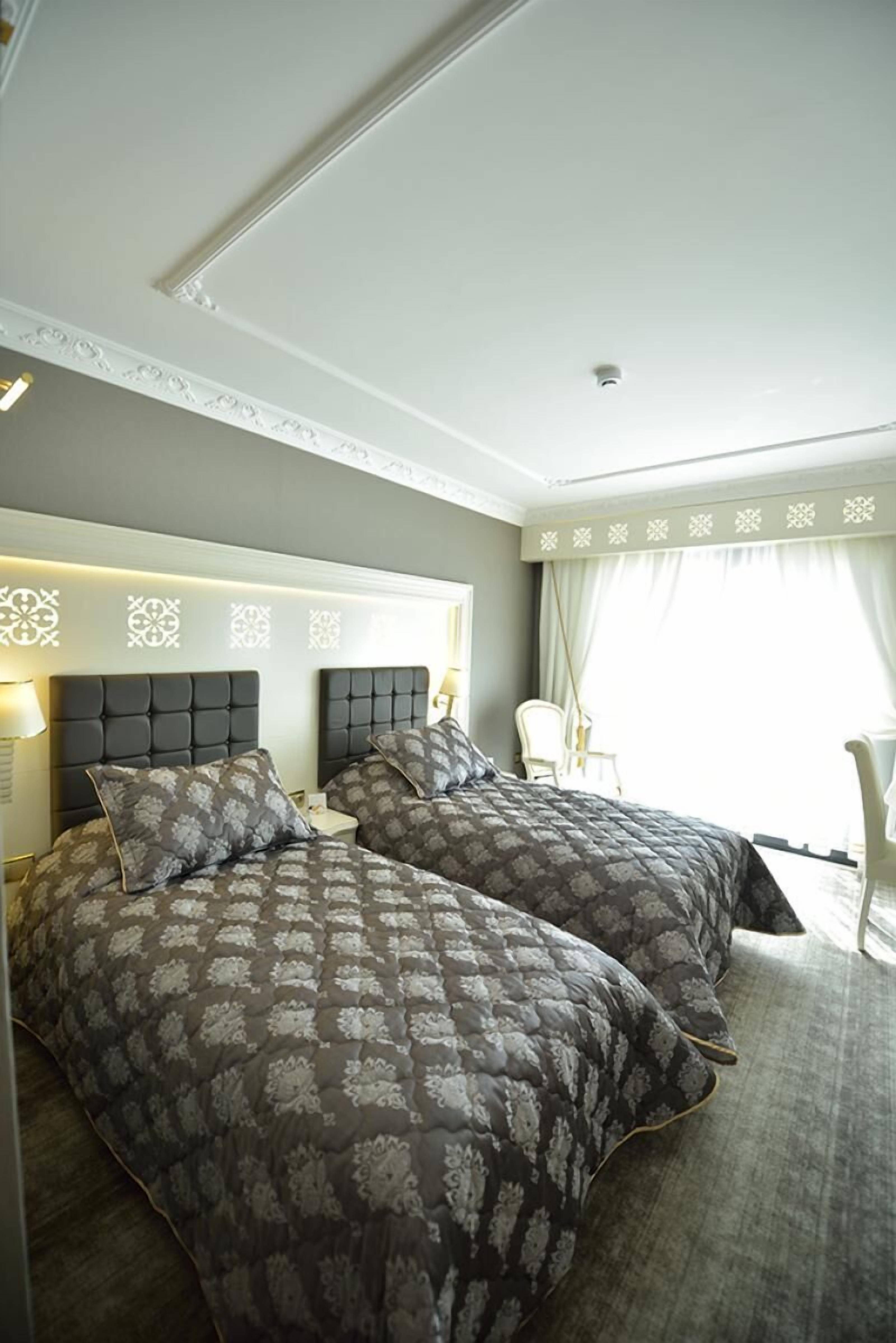A hotel room with two beds, a nightstand, a lamp, and a chair.