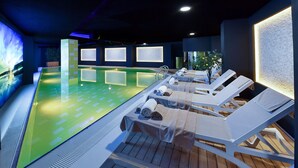 Een wellnessruimte met een zwembad, lounge stoelen en een grote muur met een digitaal scherm.