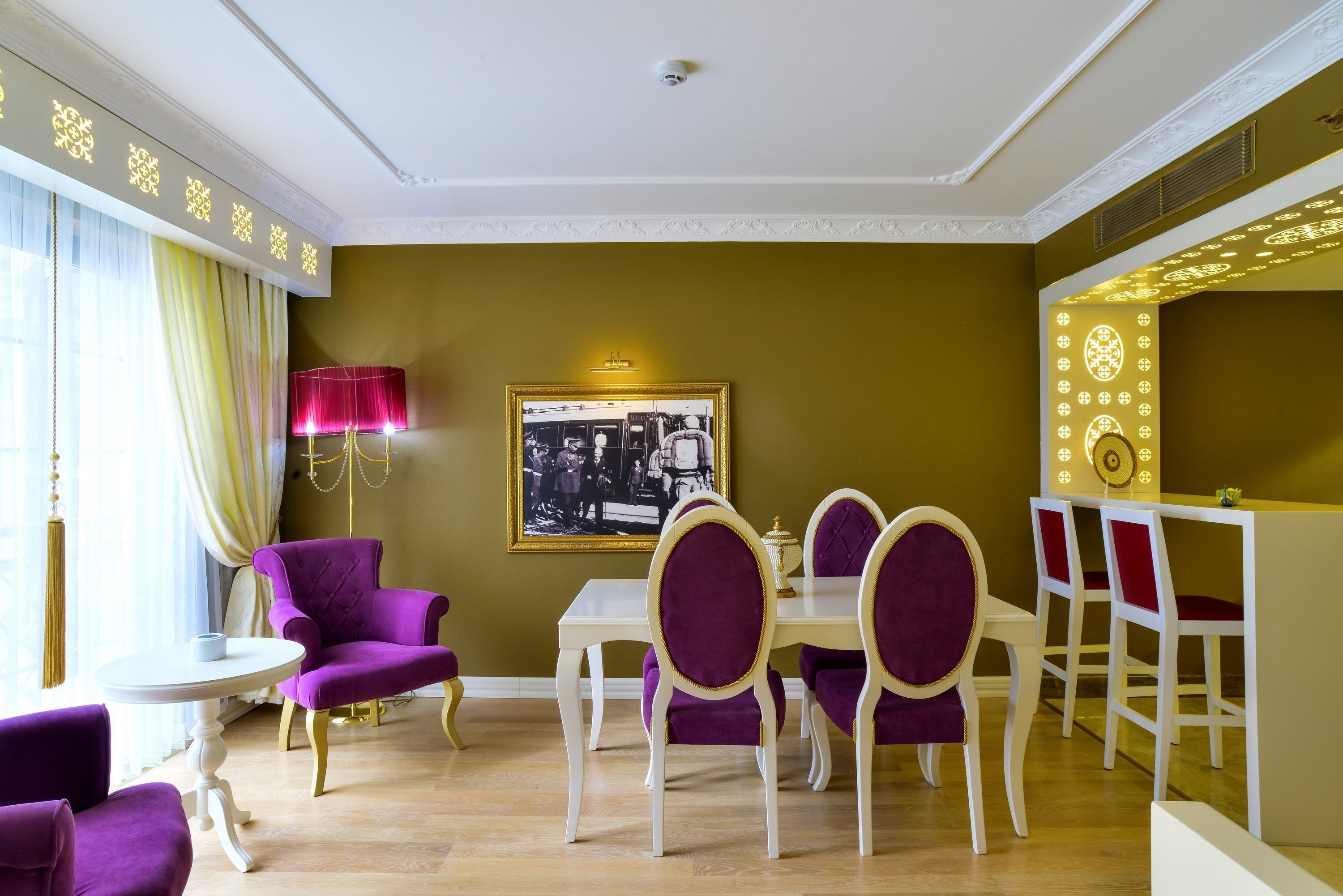 Un comedor con una mesa blanca y sillas moradas, una fotografía enmarcadas en la pared y una araña.
