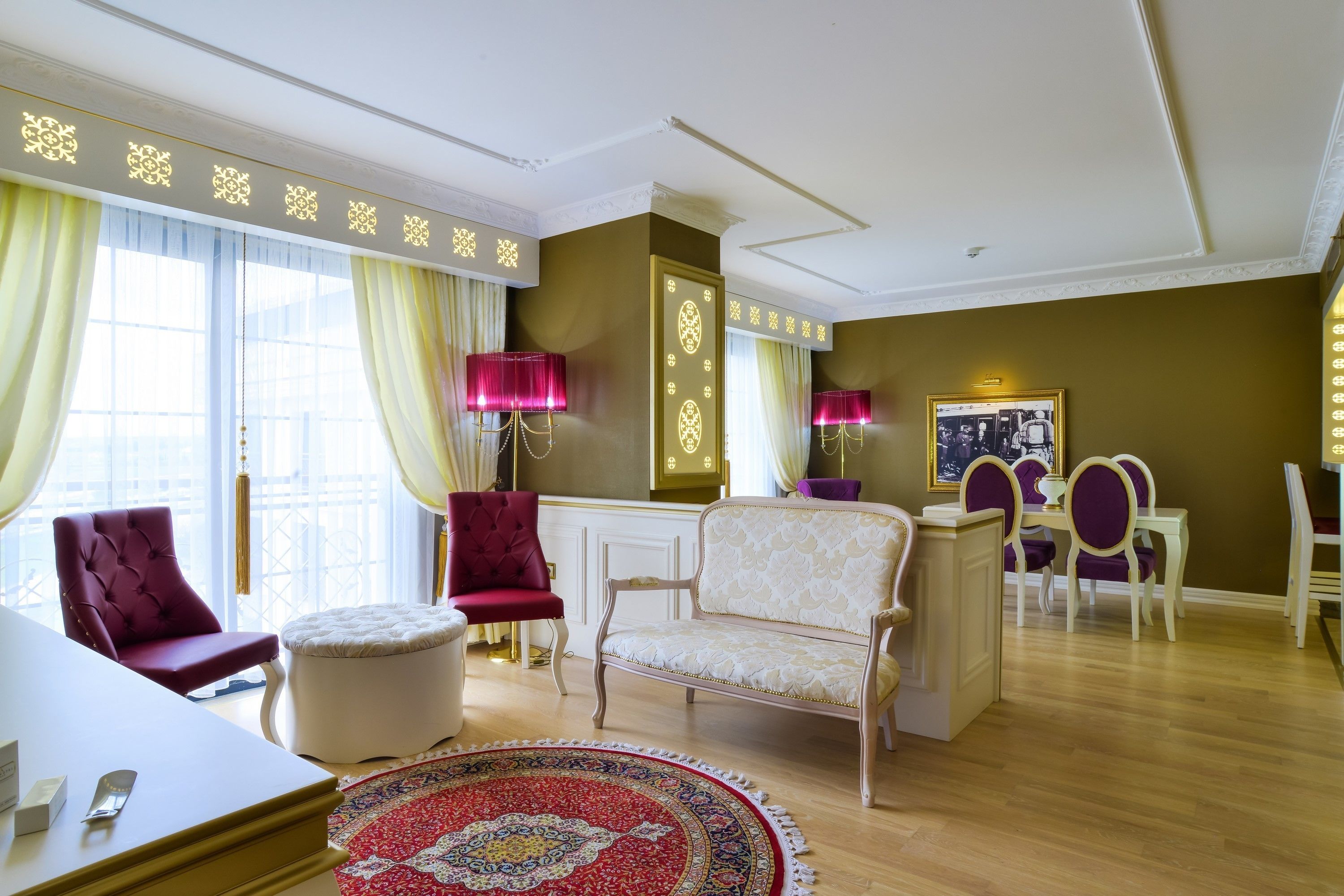 Un salón espacioso con un ventanal grande, un sofá, un sillón rojo y una zona de comedor con sillas moradas.