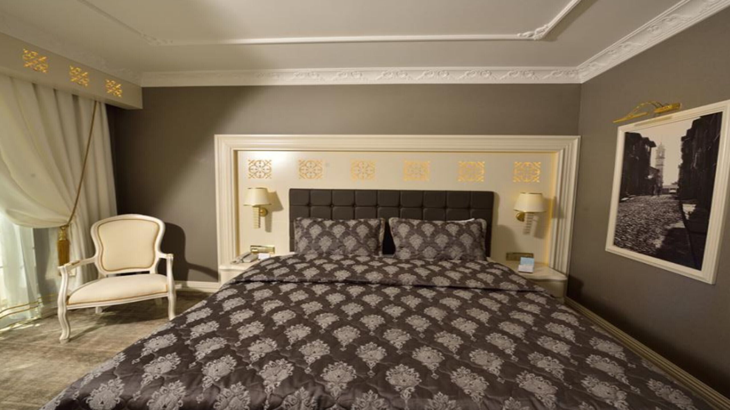 Une chambre à coucher avec un grand lit, une chaise, deux tables de chevet avec des lampes et un tableau encadré au mur.