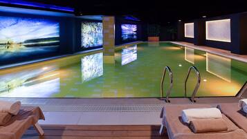 A spa pool with a tiled floor, two lounge chairs with towels, and large screens displaying nature scenes.