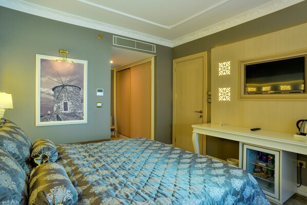 Habitación de hotel con cama, escritorio con espejo, televisor de pared y un cuadro enmarcado.