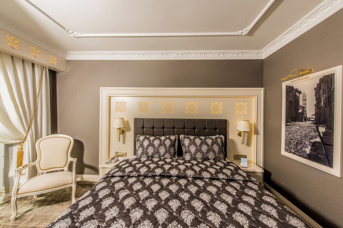 Habitación de hotel con una cama grande, una silla, dos lámparas de noche y un cuadro en la pared.