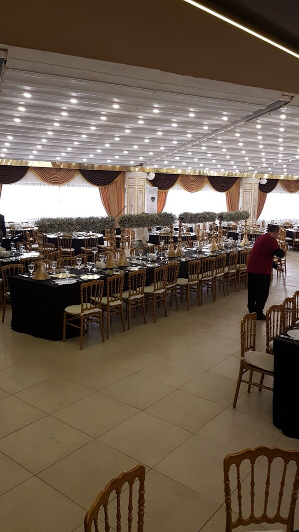 Un amplio salón de banquetes con varias mesas redondas, sillas y un techo alto con iluminación empotrada.