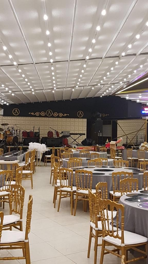 Un salón de banquetes con mesas y sillas redondas, un escenario con instrumentos musicales e iluminación empotrada en el techo.
