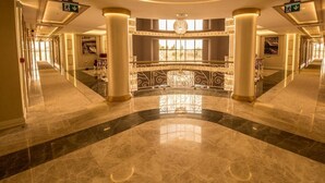 Een ruime lobby met een marmeren vloer, grote kolommen en een decoratieve balustrade in het midden.