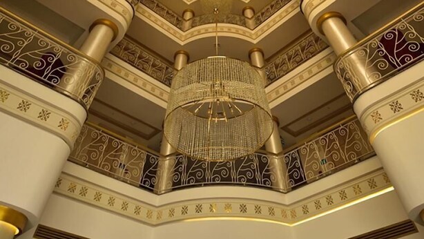Een statig, versierd interieur met een centrale kroonluchter, meerdere verdiepingen en decoratieve zuilen.