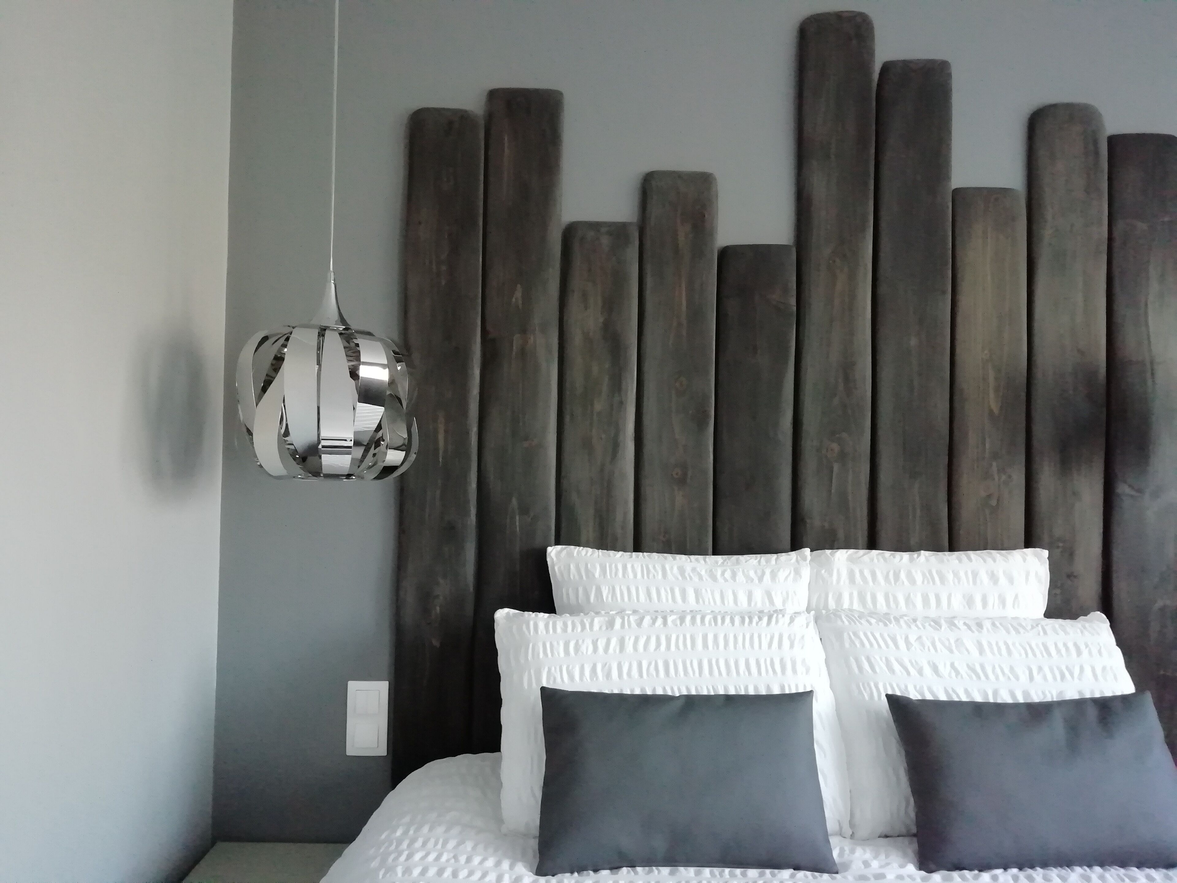Un lit avec des oreillers blancs et gris foncé, une tête de lit en bois et un luminaire suspendu.