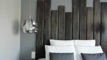 Un lit avec des oreillers blancs et gris foncé, une tête de lit en bois et un luminaire suspendu.