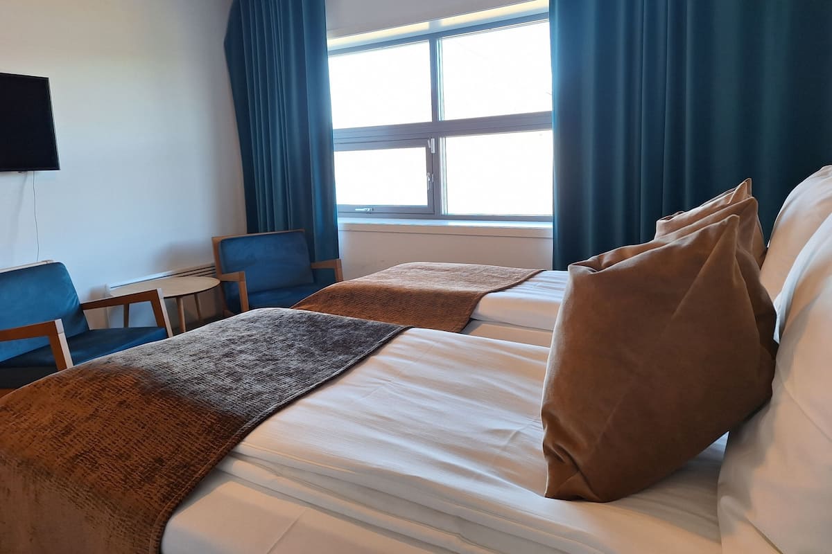 Een hotelkamer met twee bedden, een bureau, een stoel en een televisie aan de muur.