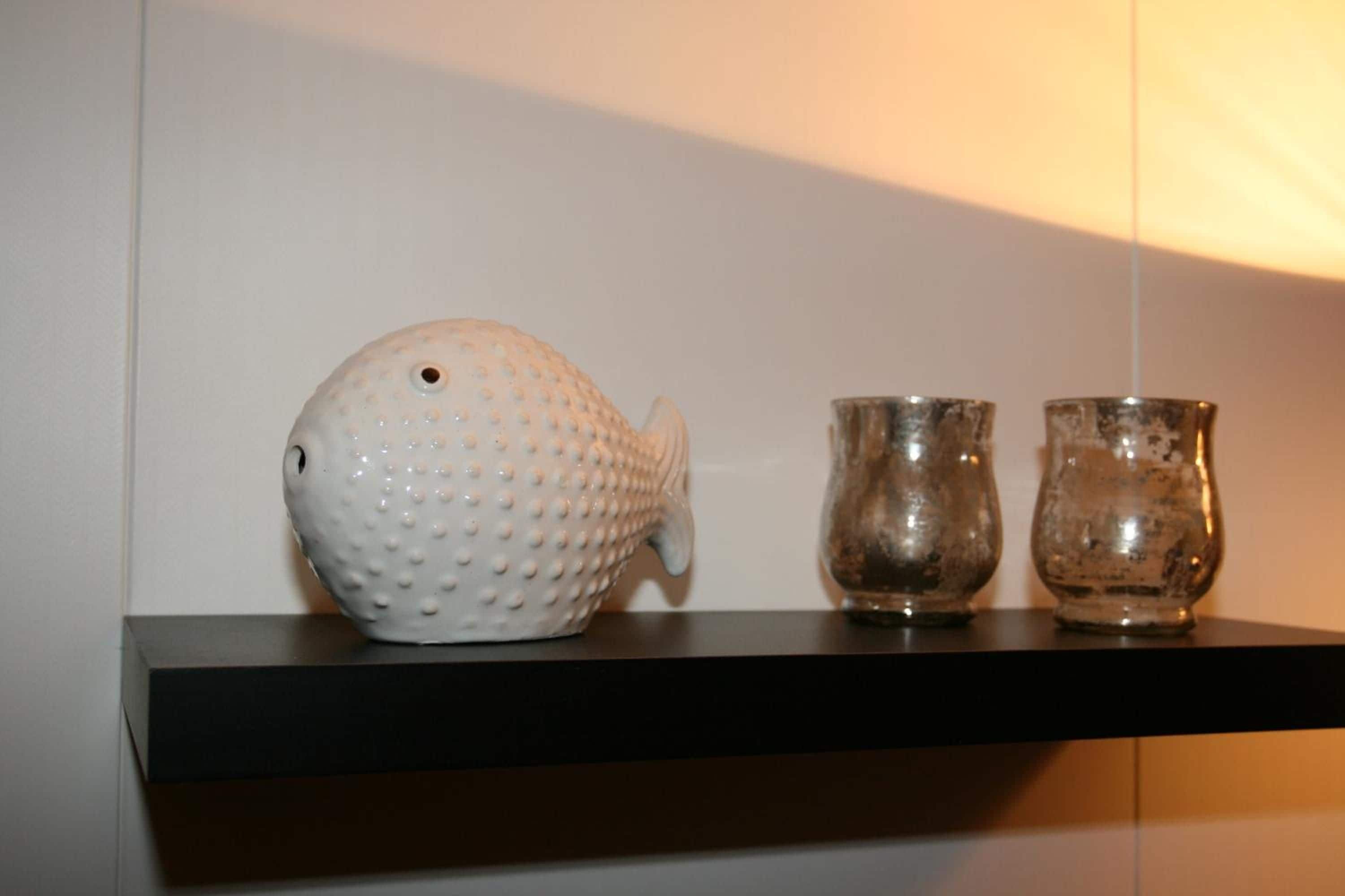 A shelf with a white textured fish-shaped object and two metallic cups.