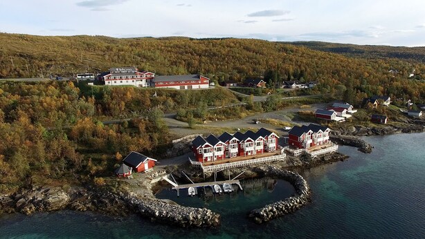 A coastal village with traditional red houses, a large building with a sign, and a dock with boats. - Tjeldsundbrua Hotel (Tjeldsund)