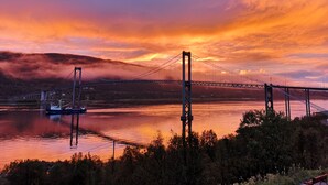 A suspension bridge over a river with a boat in the foreground. - Tjeldsundbrua Hotel (Tjeldsund)