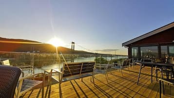 Une terrasse avec des chaises et des tables donnant sur un plan d’eau et un pont.