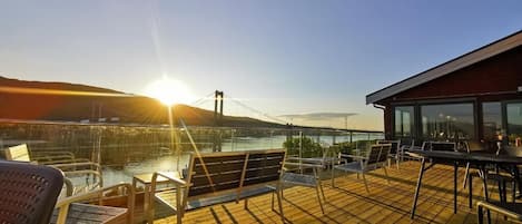 Eine Terrasse mit Stühlen und Tischen mit Blick auf ein Gewässer und eine Brücke.