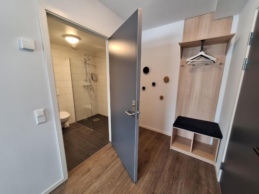A modern bathroom with a shower, toilet, and a wooden vanity with a hanging rack.