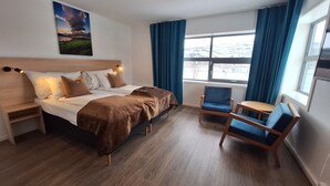 A hotel room with a bed, bedside tables, a chair, a small table, a window with curtains, and a painting on the wall. - Tjeldsundbrua Hotel (Tjeldsund)
